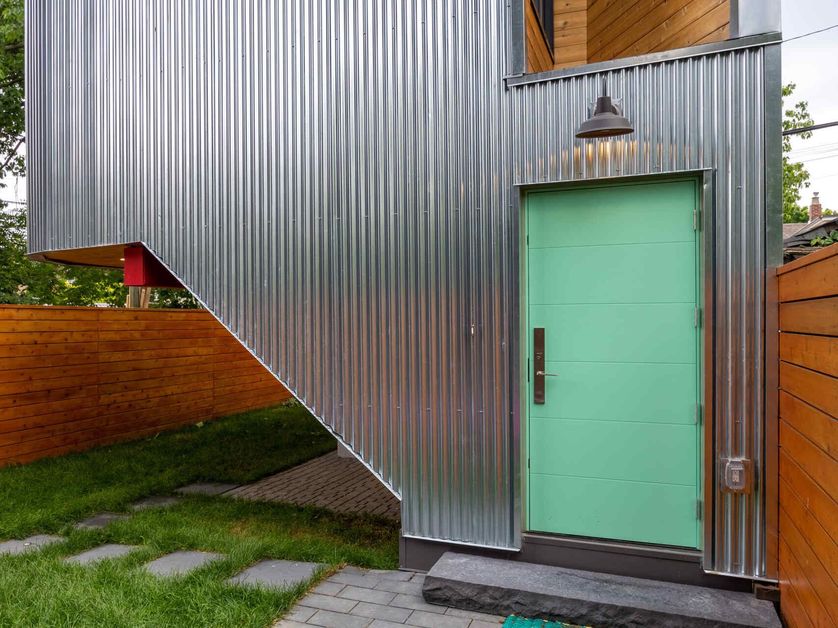 This modern laneway house, clad in corrugated metal, is also grounded in warmth. The underside of the carport is clad in cedar, and bursts of vivid accent color appear throughout the structure. These color choices reflect the clients’ affection for folk art and bring a touch of whimsy to the silvery industrial palette above.