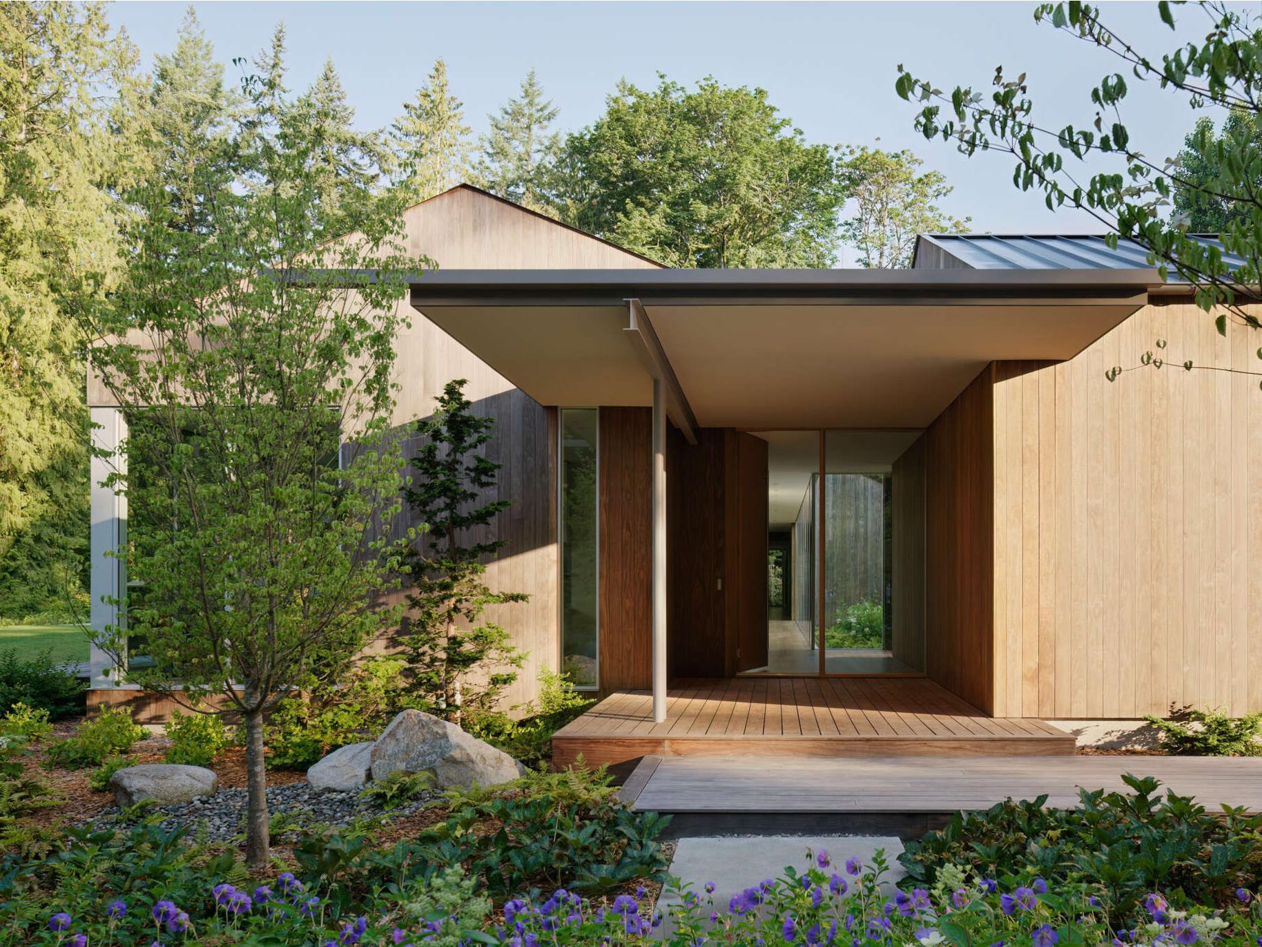 The approach to this modern home winds through preserved native trees, leading to an entry sequence made of poured-in-place concrete pavers and matching wood decking. These materials create continuity between landscape and architecture.
