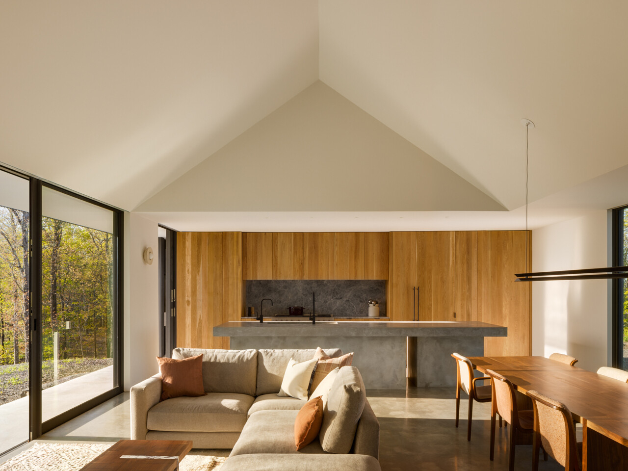 Inside, the main living space brings together the kitchen, dining area, and living room into one open-plan volume. The gabled ceiling soars to 20 feet at its peak, creating a sense of openness and calm. 