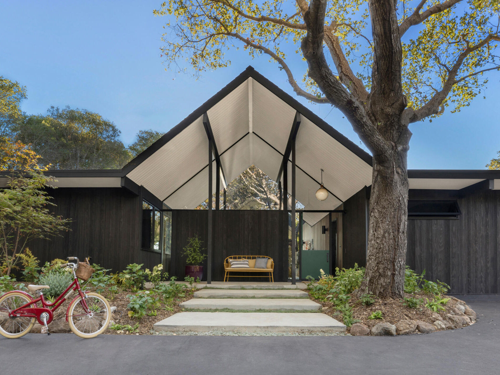 Set back from the street and accessed via a long driveway, the residence combines privacy with striking form. Its exterior has been updated using Shou Sugi Ban Accoya barn wood siding, adding texture and durability. A central gabled roof defines the structure, flanked by two flat-roofed wings that retain the home's mid-century profile.