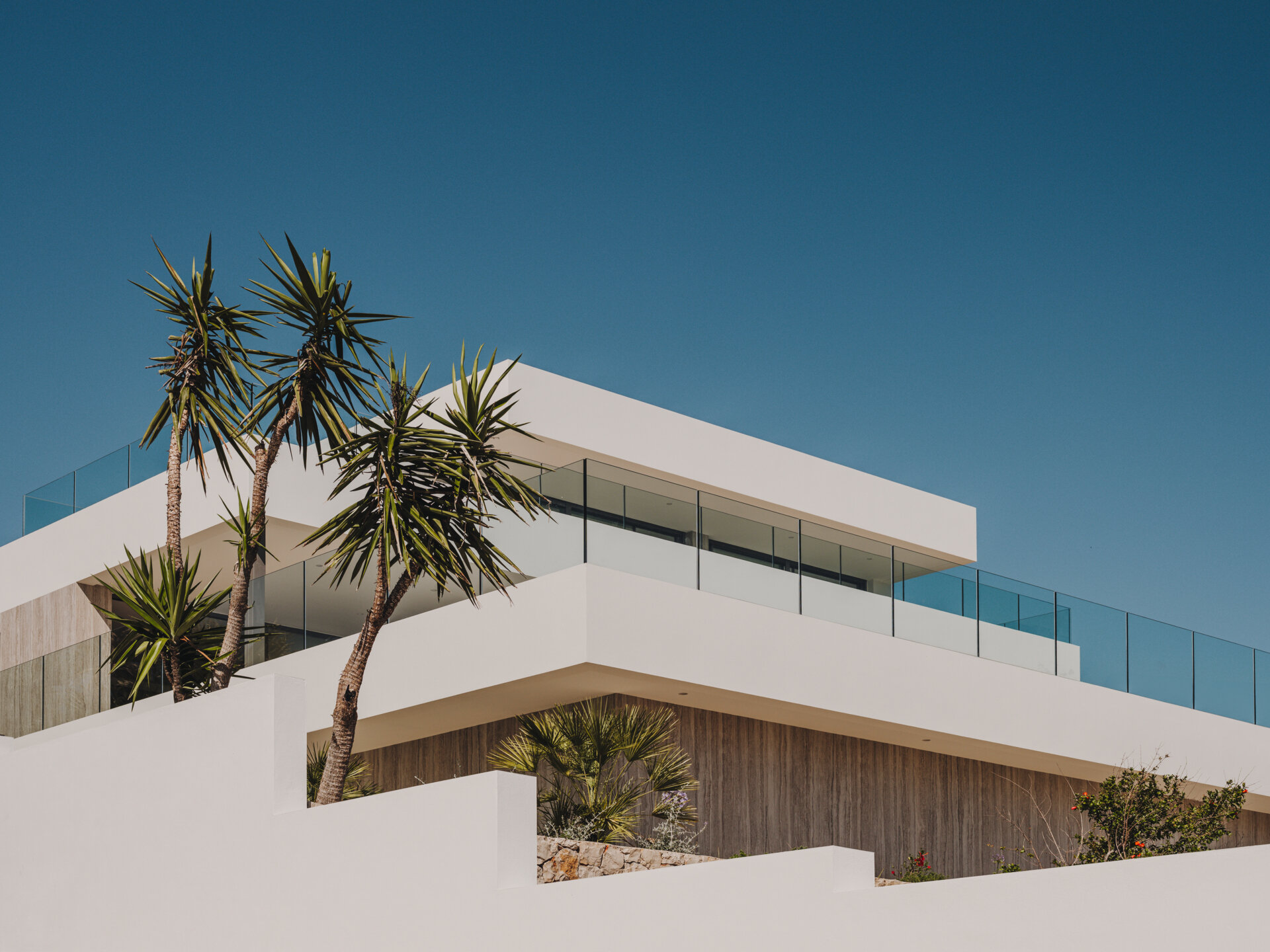 Travertine walls and oak accents define this layered coastal home that blends seamlessly into the slope.