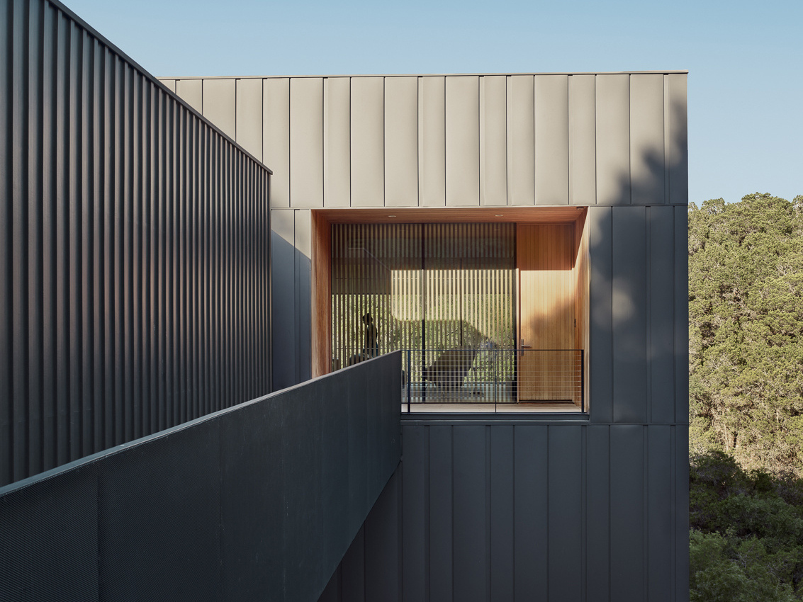 The exterior of this modern home is wrapped in vertical steel panels designed to weather, while deep wood-lined recesses frame curated views and allow light to shift throughout the day.