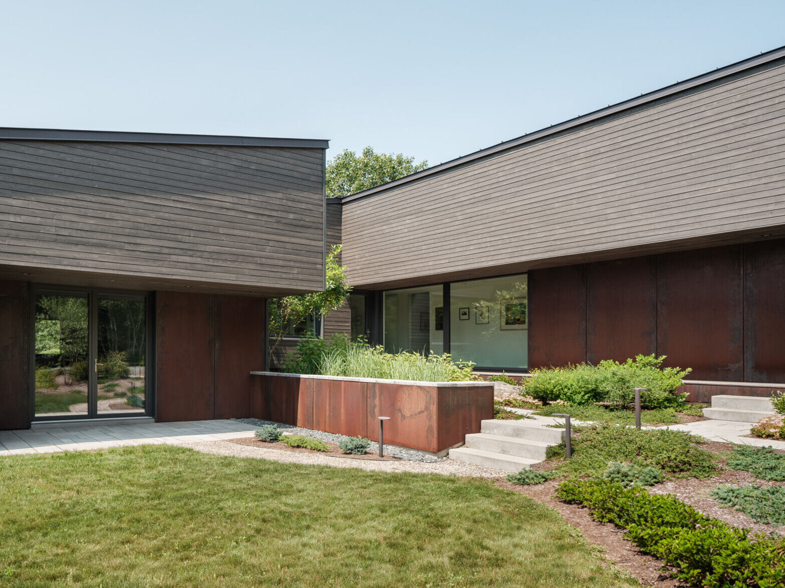 Stained cedar siding and Corten steel panels give this house a modern, grounded look that blends beautifully with the wooded riverside landscape.
