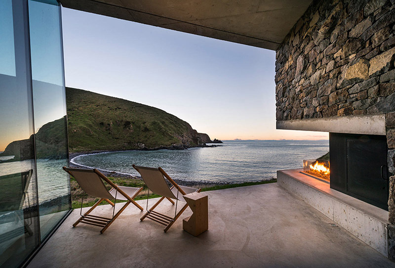 A stone cottage built using local rock, concrete, and timber to disappear into the landscape. The green roof and interlocking plan create a seamless connection with sea and sky.