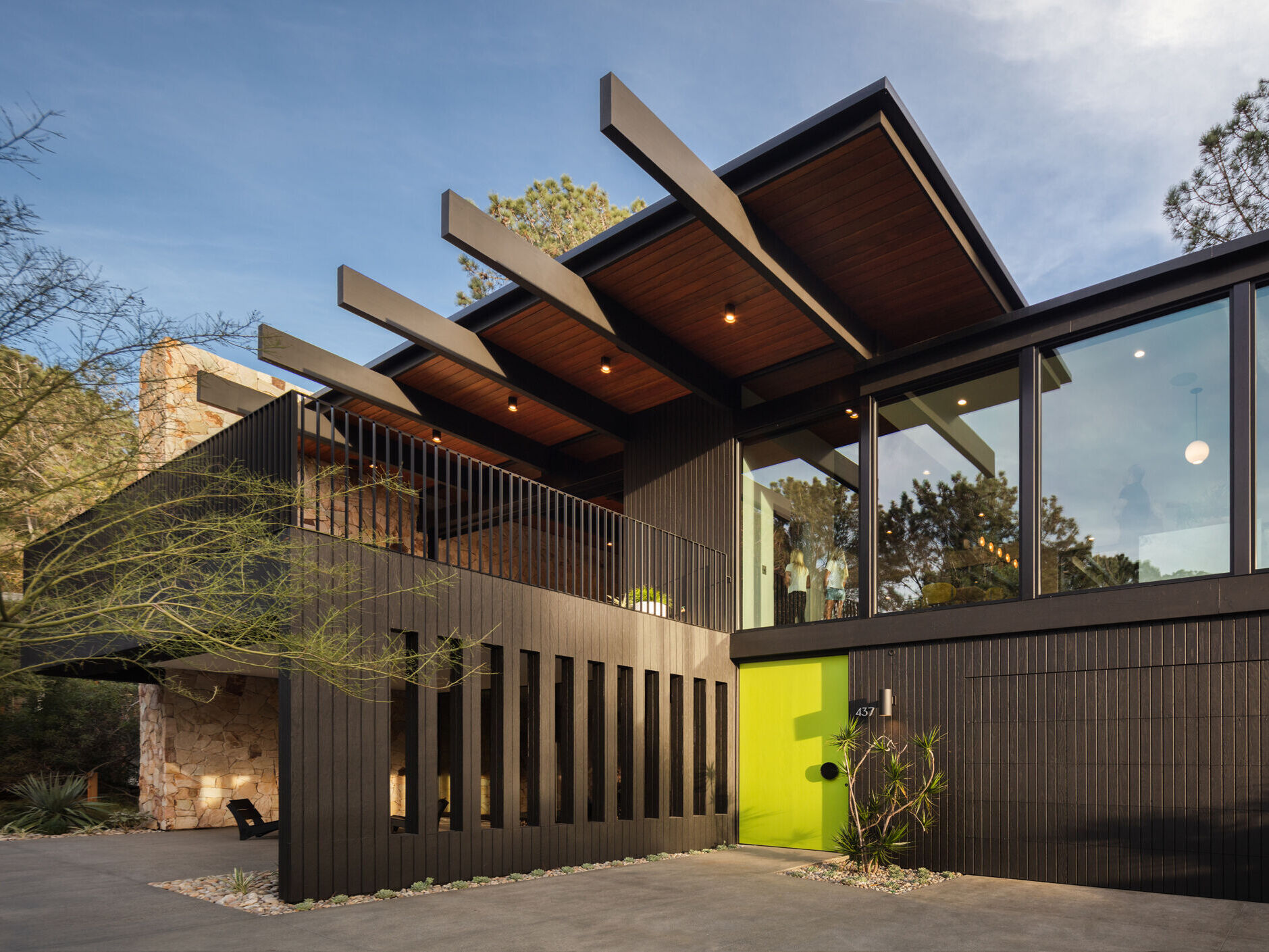 A mid-century modern inspired home with a glass, black, and stone exterior, and a bright oversized front door.