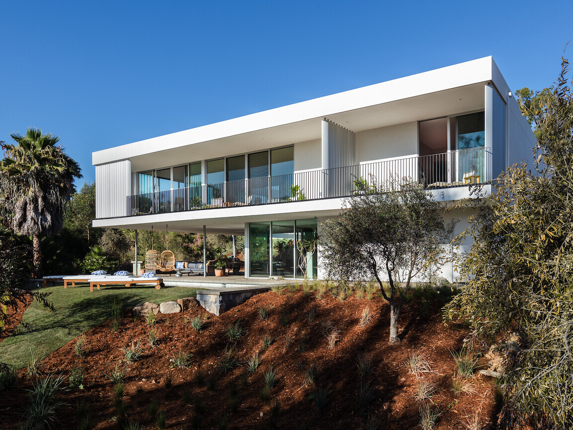 A modern house with a white exterior has a covered outdoor living room by a pool.