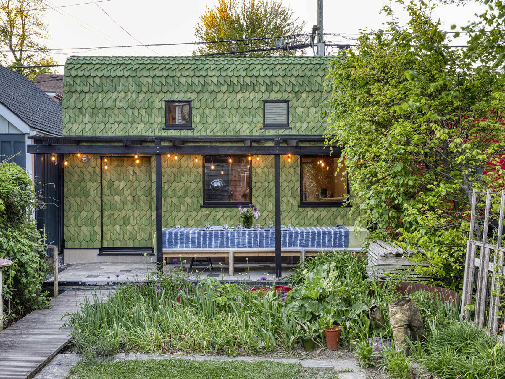 A Toronto laneway garage transformed into The Dragon, bold, playful, and full of architectural charm. It has a pergola and is covered in cedar shingles with a green pine tar finish.
