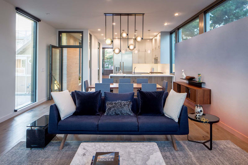 Inside this beach house, the main living, dining, and kitchen areas share one open space. A custom accent wall covered in calming wallpaper by Calico Wallpaper adds softness to the interior, while large windows flood the room with natural light.