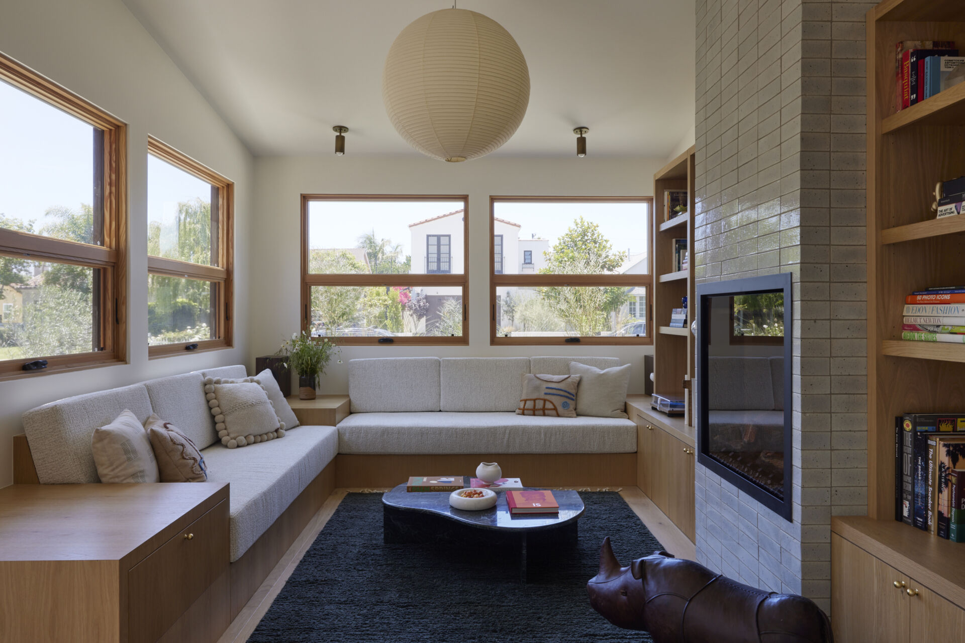 Built-in sofas, end tables, and storage make the narrow living room feel purposeful, while an electric fireplace and custom wood HVAC grille bring both style and comfort.