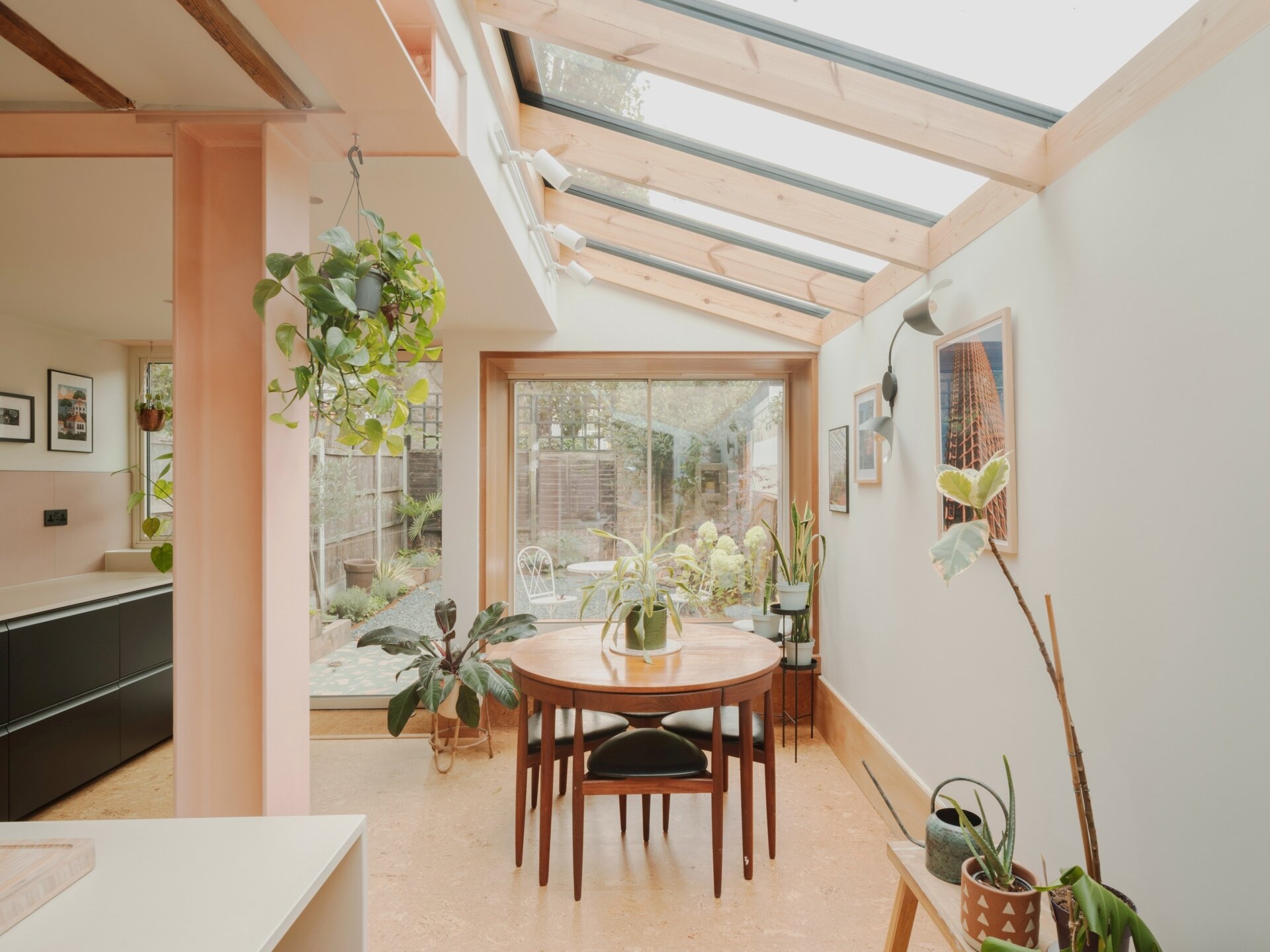 A light-filled garden extension with a new kitchen and dining area, includes pink steel, cork flooring, a pivoting door, and rooflights.