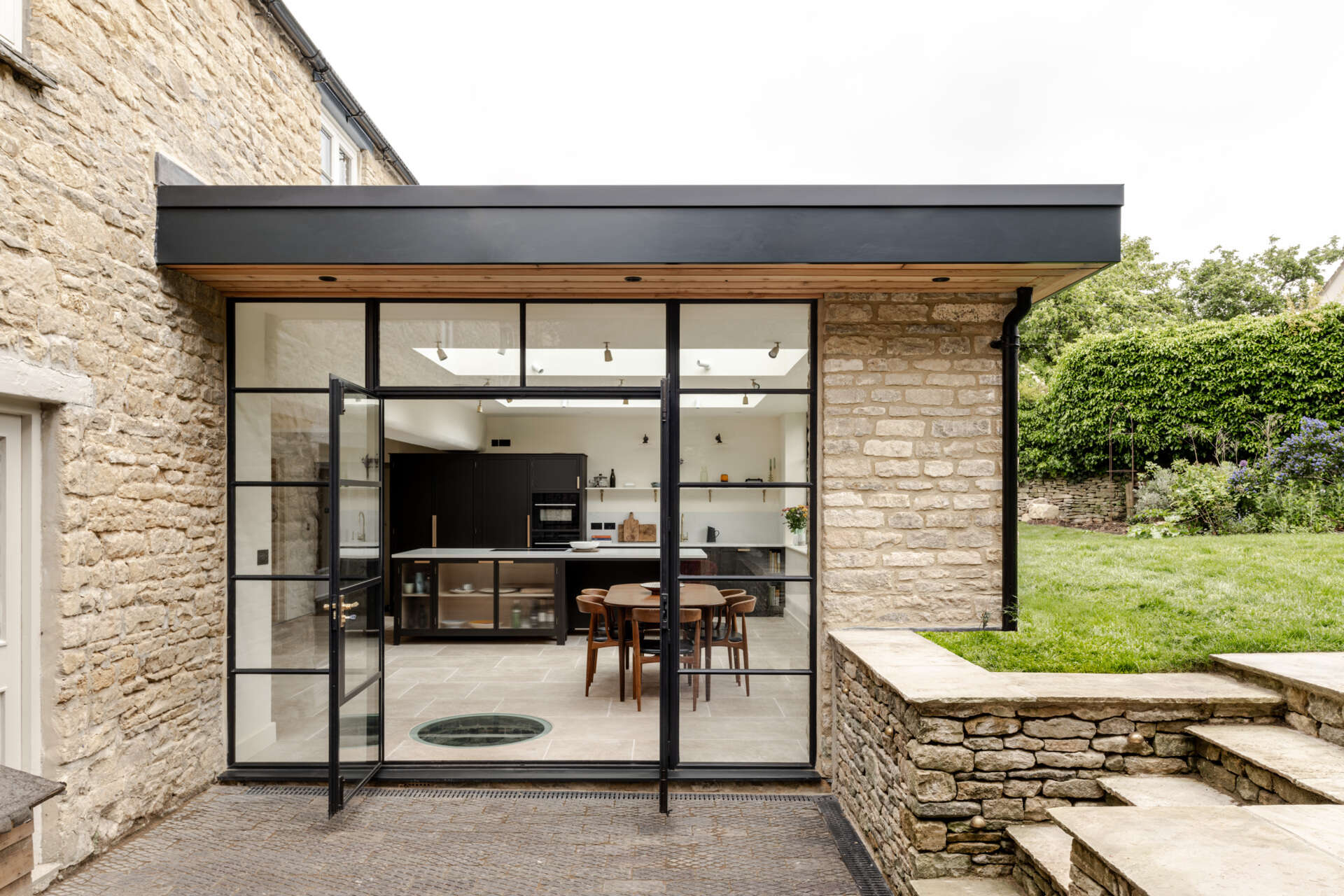 The extension sits at the rear as a low, single storey volume. By sinking it slightly into the garden, its profile stays subtle, reducing its visibility to neighbours and protecting views within the Charlbury Conservation Area. Slim steel framing, large glazing, and Cotswold stone create a gentle dialogue between old and new.