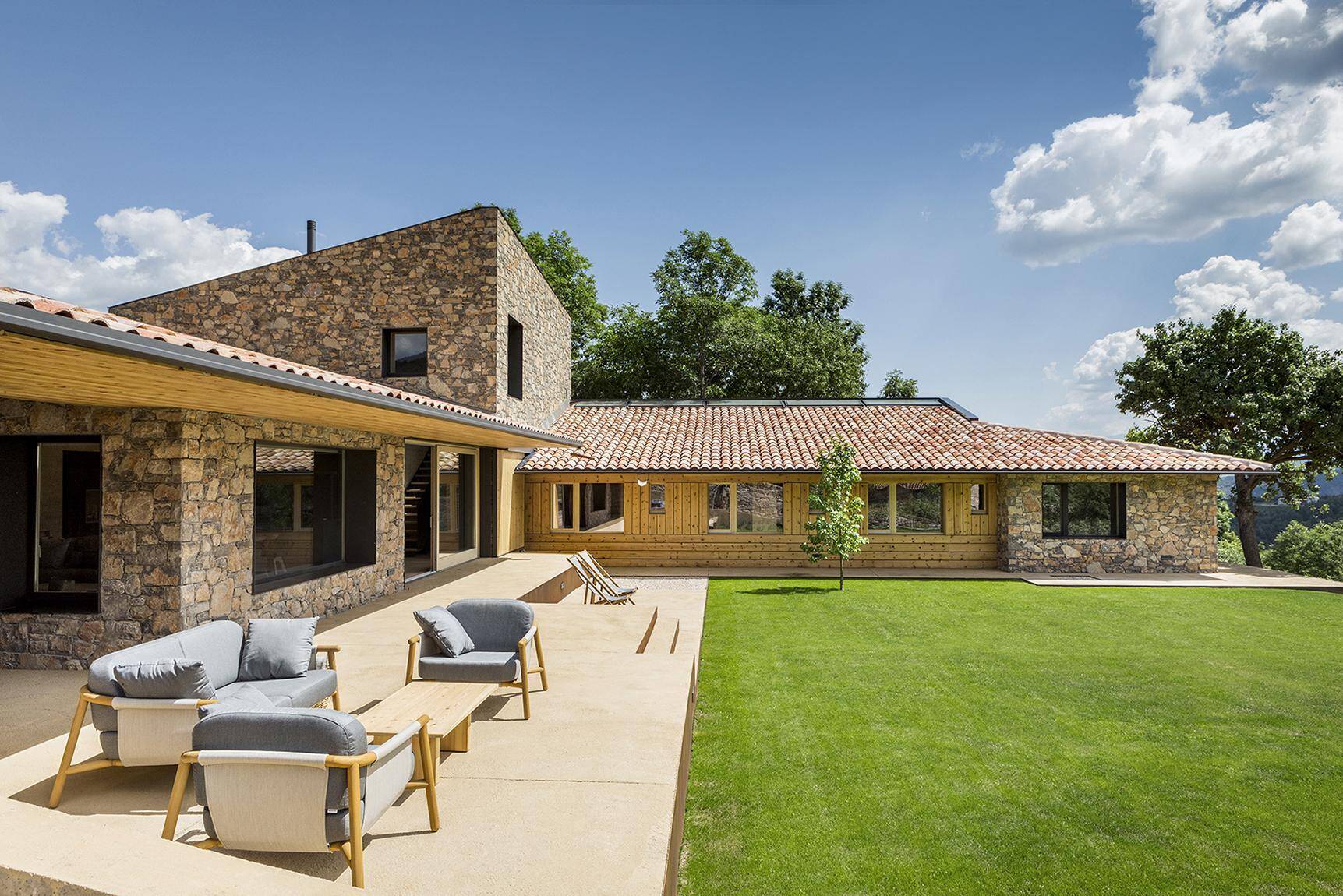 A family home in La Cerdanya designed to blend into the Pyrenees landscape using traditional stone, wood, and clay roof tiles.