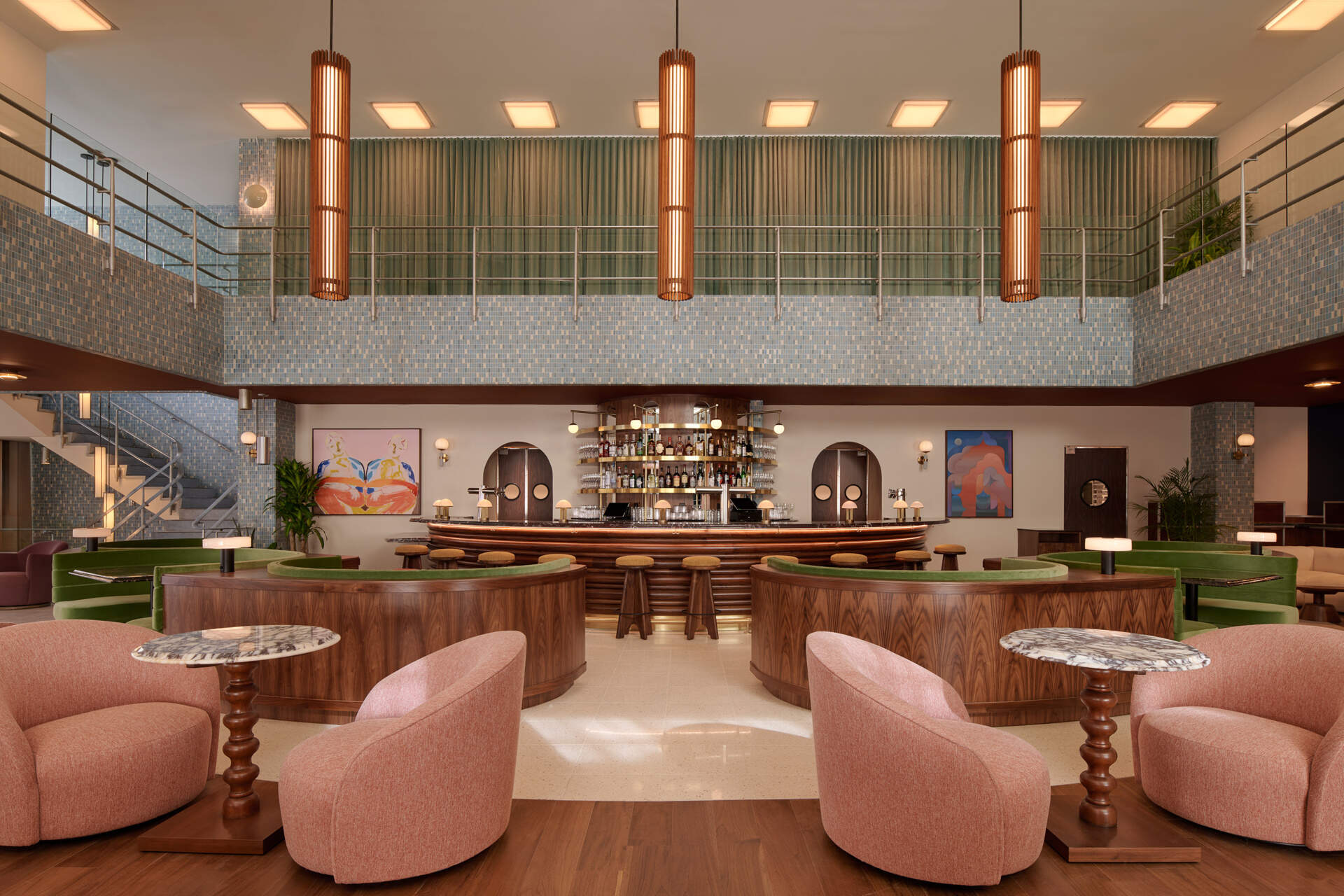 A double heighthotel lobby centers on a sculptural semicircular bar, where restored mosaic tile and mid-century lighting set the tone for gathering.