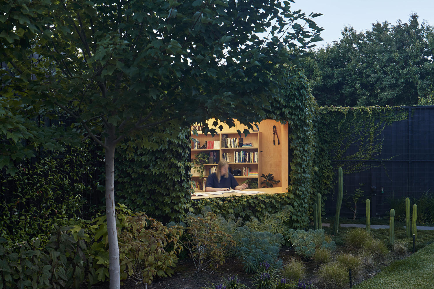 This ivy covered backyard cabin in Melbourne is a compact, peaceful workspace for creative writing. Blending seamlessly into a leafy garden, it features a plywood interior, large picture window, skylight, and sustainable design elements, offering an inspiring retreat just steps from home.