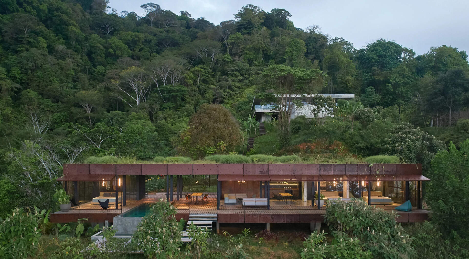 A jungle hillside home in Costa Rica disappears beneath a lush green roof, blending steel, glass and burnt timber into the surrounding forest canopy.