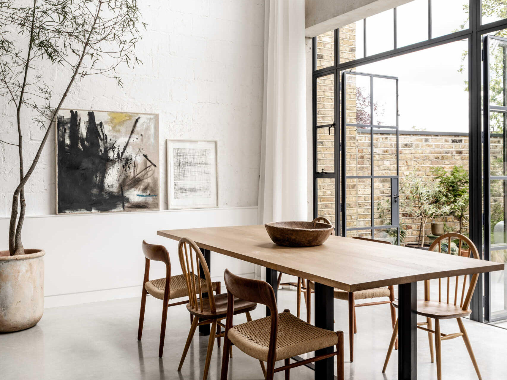 In the dining room, floor-to-ceiling glazing fills the space with natural light while framing views of the garden and the willow tree that anchors the outdoor space.