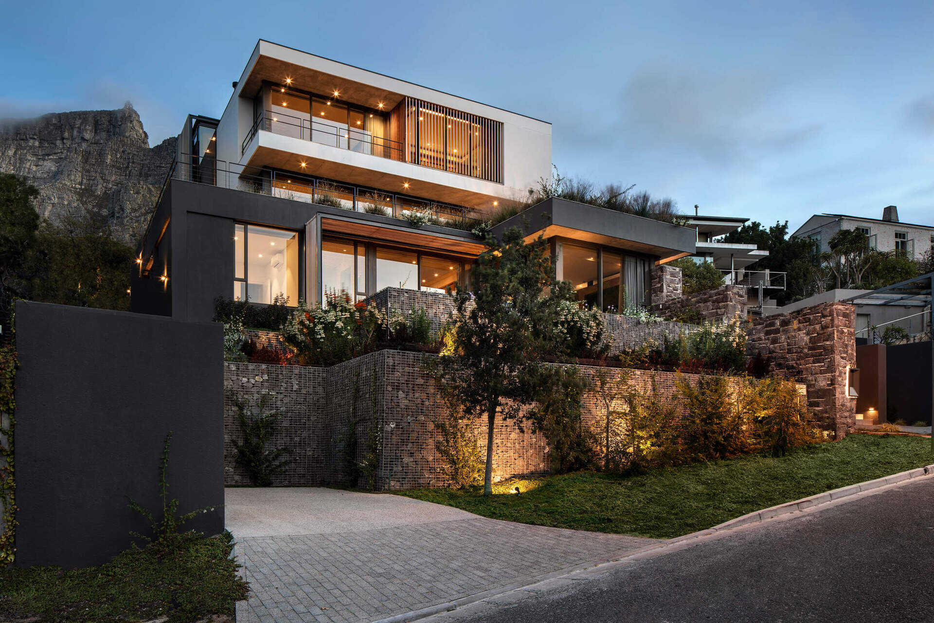 Stone and gabion walls anchor this modern Cape Town home to the mountainside, while wood slats on the upper level add warmth to the contemporary façade.