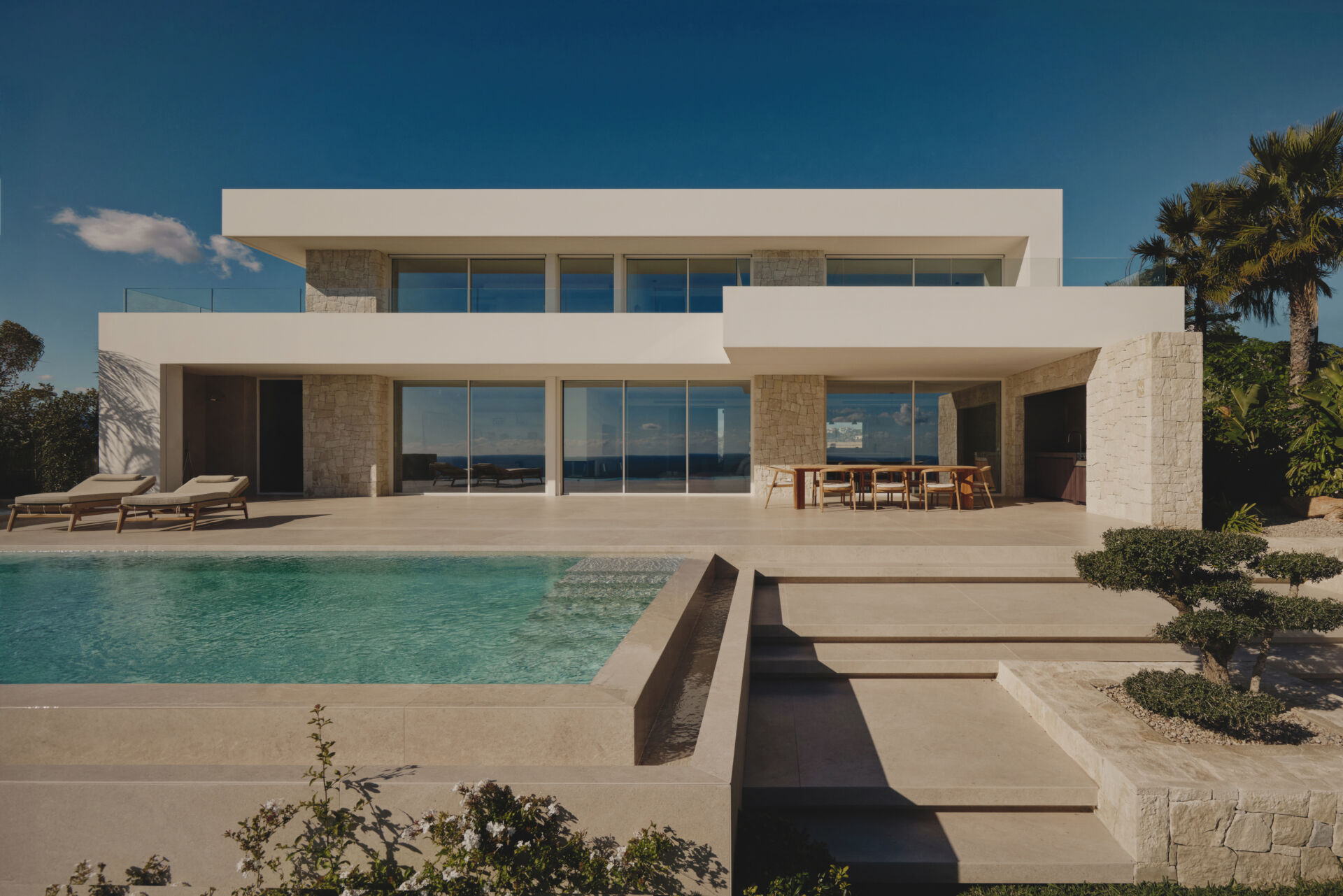 White horizontal planes rest on natural stone plinths, giving Casa L5 in Alicante a calm balance between lightness and grounded architecture.