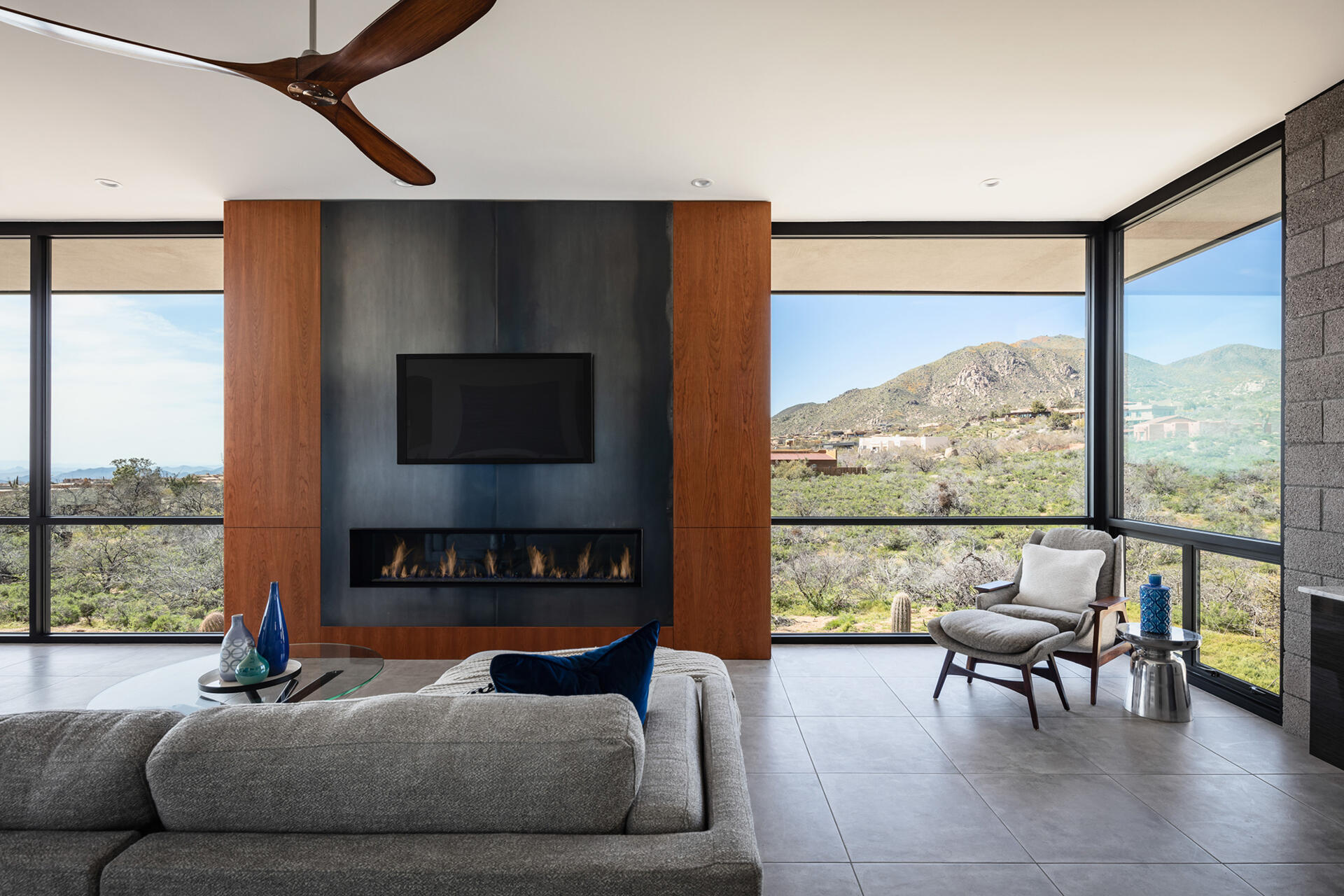 A living and dining space with warm wood cabinetry, steel accents, and full-height glass opening to the patio.