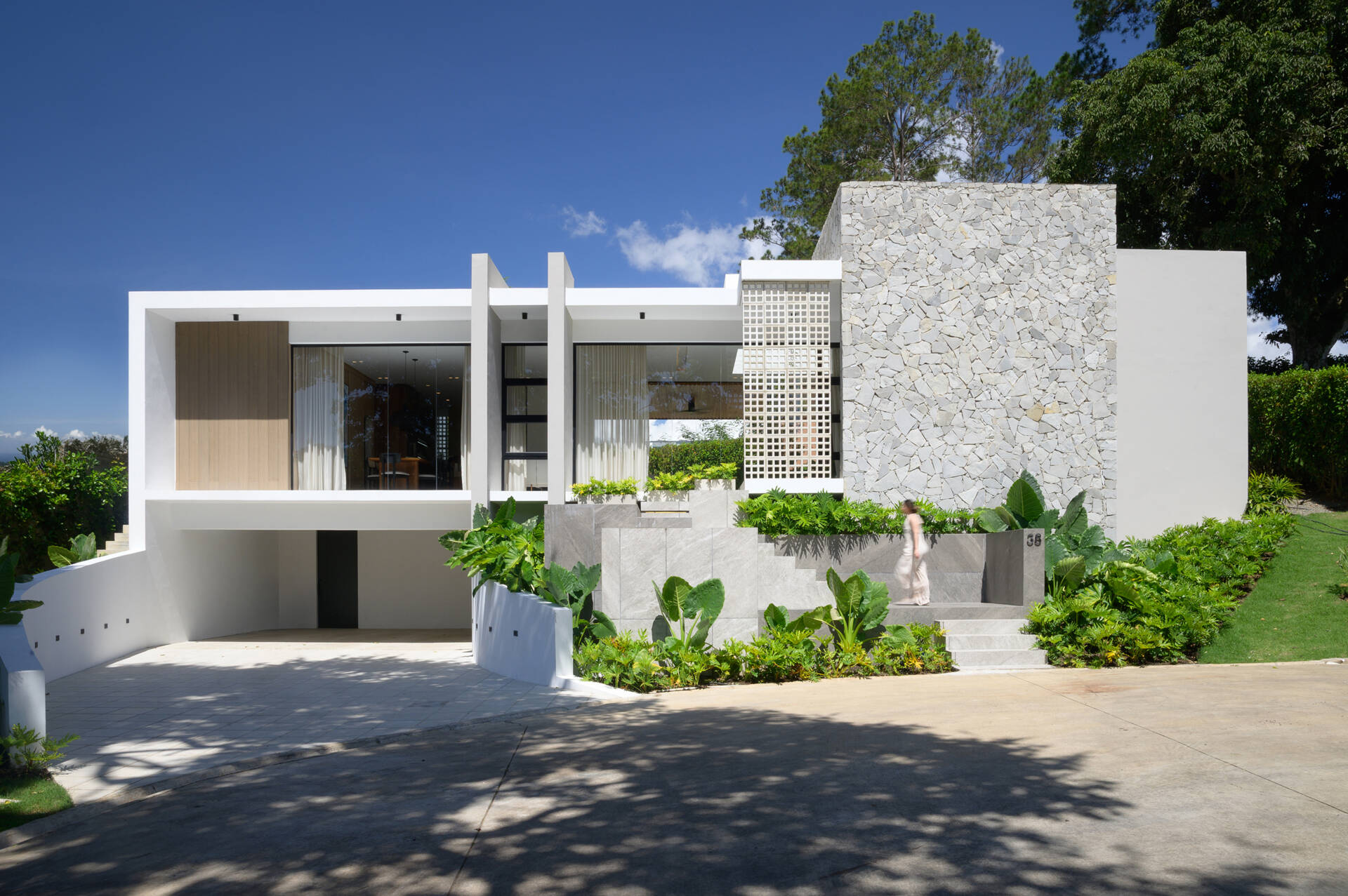 Discover how Casa L.A. uses natural stone, timber, perforated masonry and floor-to-ceiling glazing to create a modern tropical home that follows the hillside.